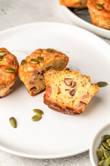 Savory zucchini muffins with ham, cheese and seeds cutted on a plate on white kitchen table background. Healthy and quick morning breakfast