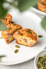 Savory zucchini muffins with ham, cheese and seeds cutted on a plate on white kitchen table background. Healthy and quick morning breakfast