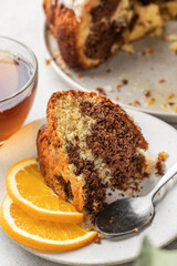 Piece of orange and chocolate marble bundt cake with sugar icing close up. Fruity citrus dessert on light gray kitchen background