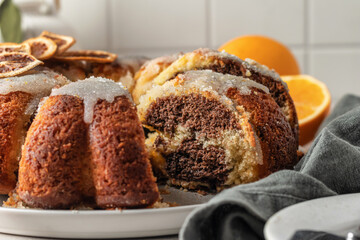 Sliced orange and chocolate bundt cake with sugar icing. Fruity citrus dessert on light gray kitchen background