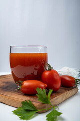tomato juice in a glass on a wooden board on a white background with cherry tomatoes