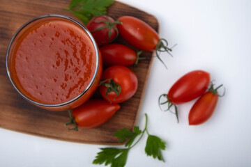 tomato juice in a glass on a wooden board on a white background with cherry tomatoes