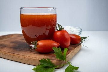 tomato juice in a glass on a wooden board on a white background with cherry tomatoes