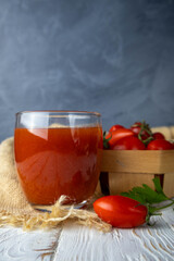 Tomato juice in a glass on a wooden rustic table with cherry tomatoes on grey background