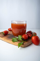 tomato juice in a glass on a wooden board on a white background with cherry tomatoes