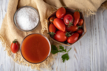 Tomato juice in a glass on a white wooden rustic table with cherry tomatoes