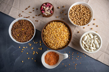 Variety of protein-rich legumes in different bowls on a gray background with free space