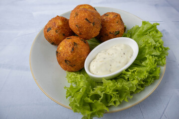 Fried potato balls served on a plate with sauce and a lettuce leaf
