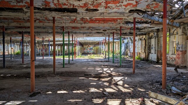 Derelict disused factory. Abandoned old industrial warehouse vibrant colours, peeling paint ceiling, sunlight shadows. Decaying construction building interior columns. Empty crumbling structure ruin.
