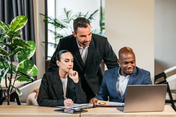 Group of diverse business professionals collaborating in a modern office space, analyzing data on a laptop, surrounded by greenery and contemporary decor, showcasing teamwork and innovation