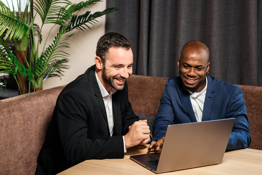 Two professional men engaged in a collaborative discussion while working on a laptop at a modern office space, showcasing teamwork and innovation in a business environment