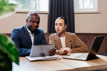 Businessman and businesswoman engaged in a collaborative discussion while reviewing data on a tablet, with a laptop and modern office setting enhancing the professional atmosphere