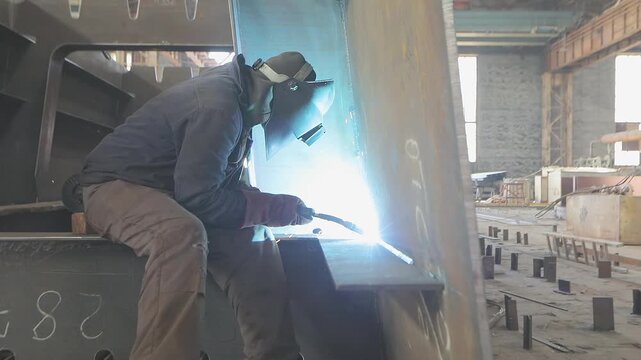 Welders welding large steel sections steel box girder of bridge. Welders weld large steel sections of a bridge's box girder. Shipbuilding factory. Manufacturing plant. Indoor