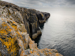 Mini cliff in county Clare, Ireland. Rough Irish stone coast in Burren area. Calm Atlantic ocean and cloudy sky. Popular tourist area.