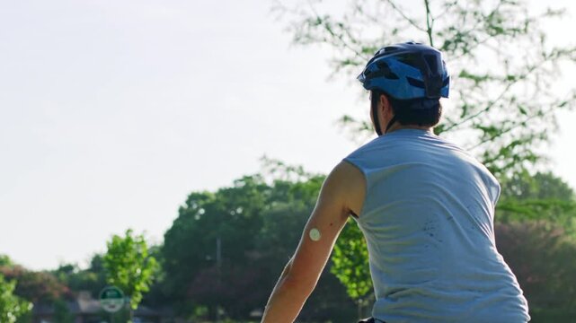 Shot of a cyclist with a diabetes monitor on his arm riding through a park on a sunny day.