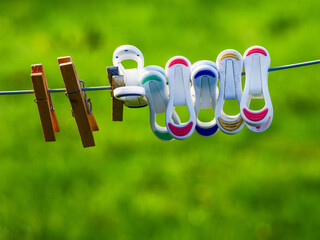 Old style wooden and new colorful fancy cloth pegs on a string in a yard outdoors. Green field background out of focus.
