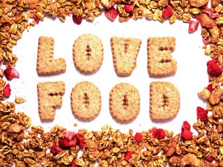 Word love food with letters made from cookie on white background framed by granola cereal with dried strawberry. Top down view. Promoting healthy food theme.