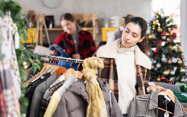 Obraz premium Armenian woman stands in a Christmas shop and chooses jackets, coats and down jackets among winter outerwear. Shopping for the family before the New Year and holidays