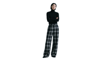 A woman in a black turtleneck and plaid wide - leg pants stands with arms crossed, showcasing a modern fashion look.