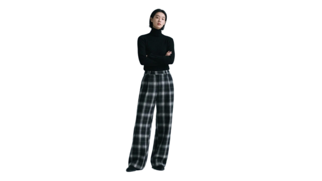 A woman in a black turtleneck and plaid wide - leg pants stands with arms crossed, showcasing a modern fashion look. - Powered by Adobe