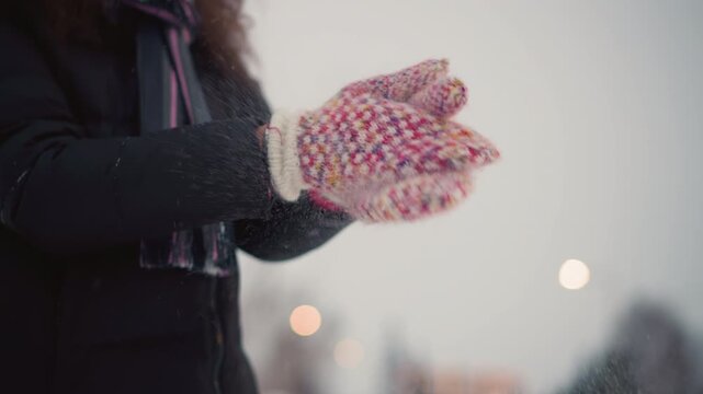 Skater wearing colorful knitted mittens claps hands outdoors during cold winter day, snowflakes scattering from wool texture, creating cozy seasonal scene with warmth, movement and festive winter
