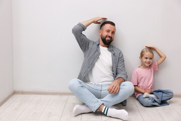 Father and daughter measuring their heights near light wall indoors. Space for text