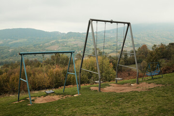 Fototapeta premium Multiple swings placed on a hill with a panoramic view of mountains and valleys under cloudy sky. Ideal for travel, recreation, and freedom concepts