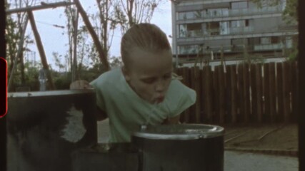 Filmed on super 8 film - youthful girl drinking water from fountain in a playground during sunny summer day, capturing nostalgic vintage moment of carefree childhood in urban playground