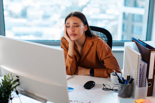 Bored upset European businesswoman looking at computer screen, sitting in office and feeling tired and sad