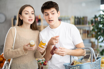 Couple young man and woman buyers chooses red and yellow smoothie in bottle in grocery store