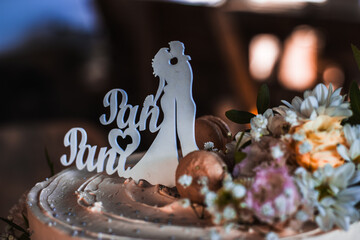 Close-up of a romantic wedding cake topper featuring a bride and groom silhouette surrounded by fresh flowers and macarons, symbolizing love and celebration.