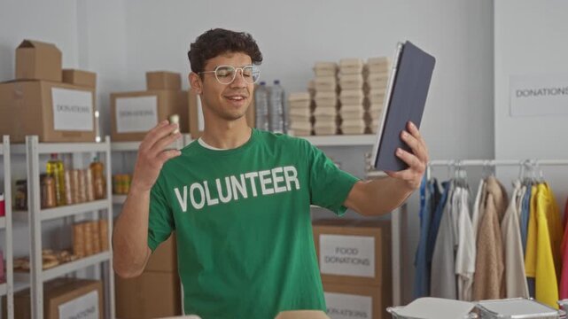 Man holds a tablet and waves hand while standing among donation boxes in building donation center; compassion generosity joy.