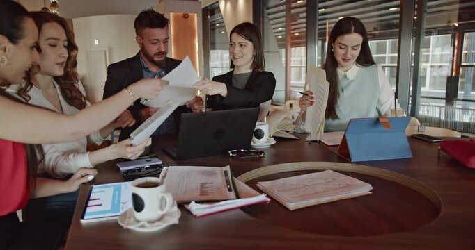 Business colleagues gather in a vibrant office cafe, collaborating on documents and reports while enjoying coffee and conversation.