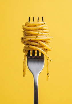 A silver fork impales vibrant yellow spaghetti, showcasing its texture against a solid yellow background in a minimalist style.