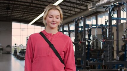 Portrait of a confidant young female athlete in a pink hoodie with weights in the background.