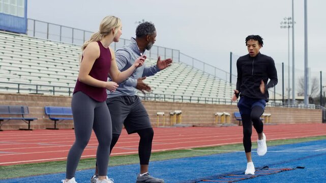 Coaches instruct a young athlete during an agility training session on an outdoor track.