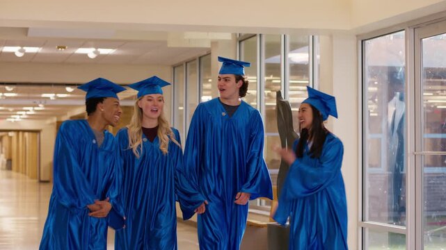 New graduates walk together down a hallway in blue caps and gowns