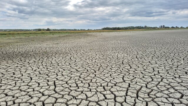 Dry, cracked earth under a cloudy sky, symbolizing drought, climate change, and environmental crisis. Desolate landscape of parched land.