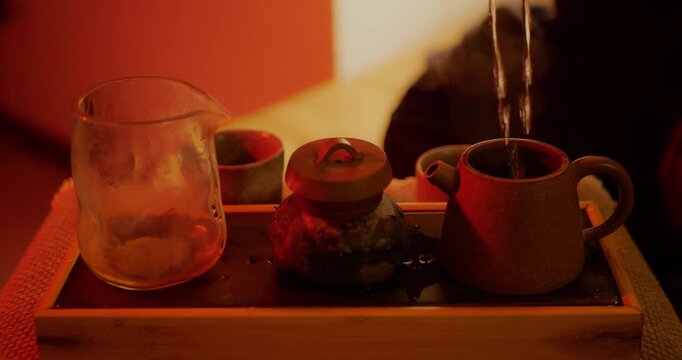 Steaming hot water pours into a ceramic teapot on a wooden tray under warm, ambient light. Cozy beverage ritual, relaxation, and Chinese tea-making concept in a tranquil indoor setting.