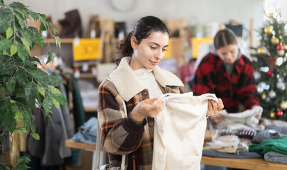 Armenian woman stands in a store against the background of a Christmas tree and chooses warm pants for the winter holidays. Buyer on sale before Christmas and New Year, holiday atmosphere around