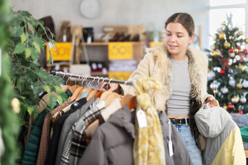Glad young woman holding a hanger with puffer jacket in retail outlet during X-mas sell-out