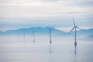 Offshore wind turbines in calm sea with misty sky, representing renewable energy and sustainable power generation.