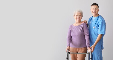 Young caregiver with senior woman on grey background with space for text