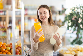 Young woman buyer chooses bottle of soda in grocery store
