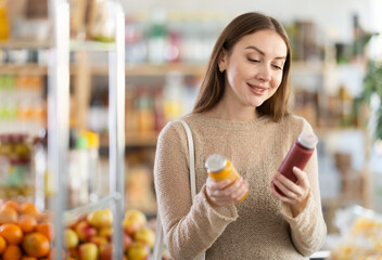 Young woman buyer chooses red and yellow smoothie in bottle in grocery store