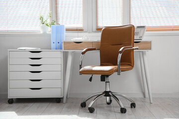 Comfortable workplace with leather brown chair near window in room, closeup