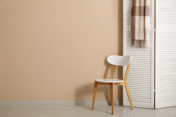 Folding screen and chair near beige wall in room, closeup