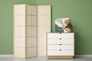 Folding screen and chest of drawers near green wall in room