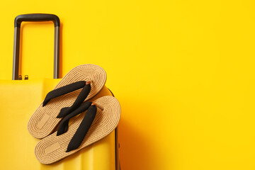 Suitcase and flip-flops on yellow background, closeup