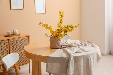 Vase with blooming branches on table near beige wall in interior of dining room, closeup